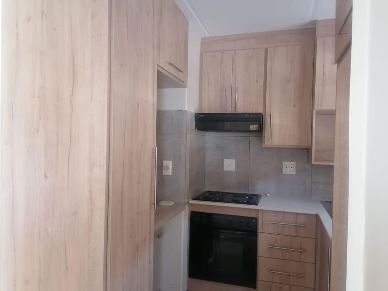 A compact, modern kitchen featuring light wood-grain cabinetry, integrated electric oven and hob, extractor fan, and neutral tiled backsplash.