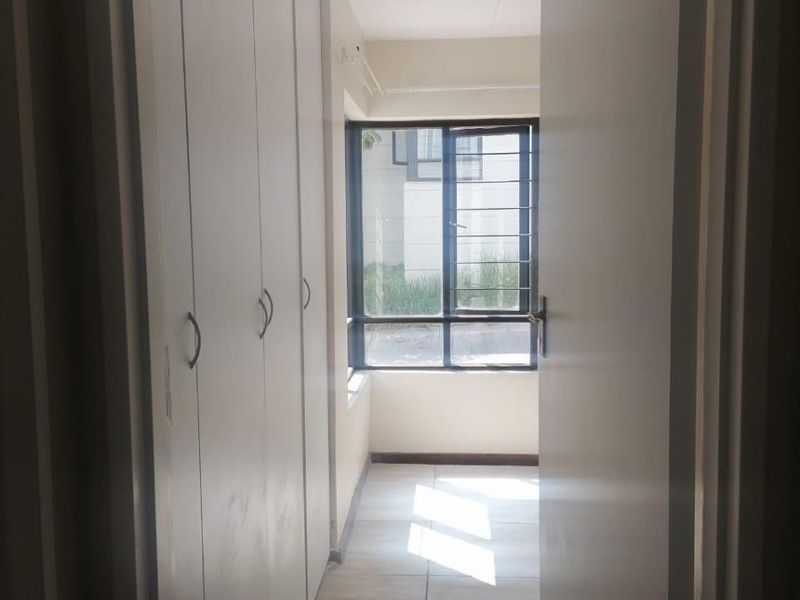 A bright, empty bedroom featuring built-in cupboards, tiled flooring, and a window with security bars, offering a clean and functional space.