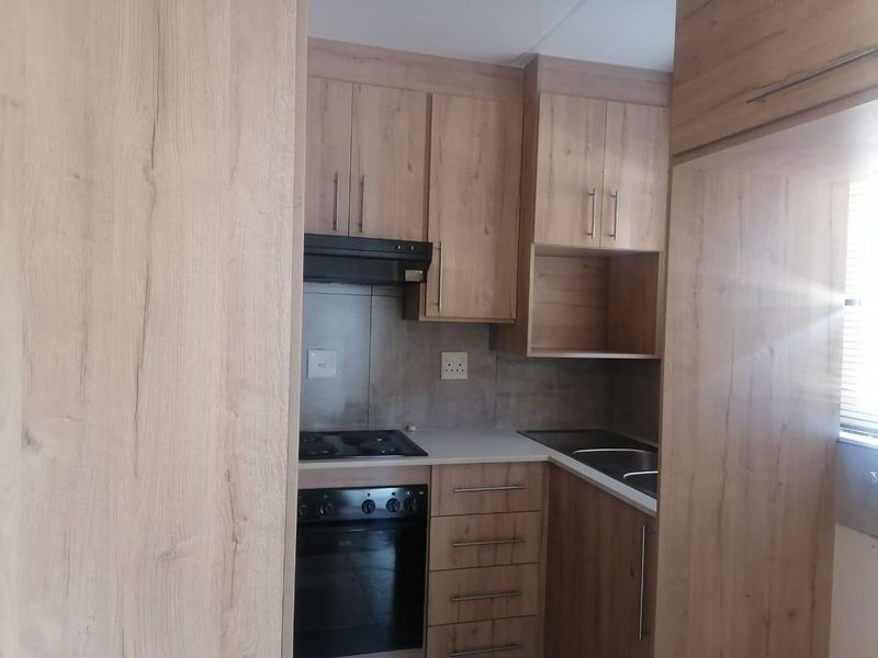 A compact, modern kitchen featuring wood-look cabinetry, integrated appliances including an oven and hob, and a functional tiled backsplash.
