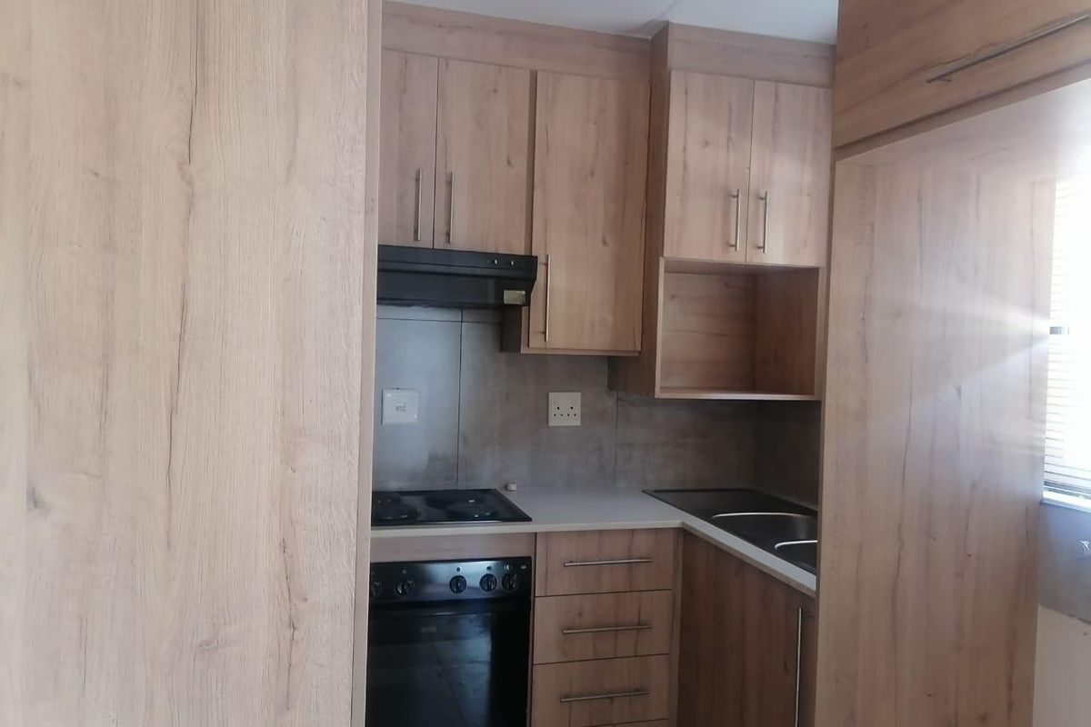 A compact, modern kitchen featuring wood-look cabinetry, integrated appliances including an oven and hob, and a functional tiled backsplash.