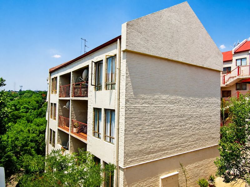 A side and rear view of a multi-story apartment building featuring a painted brick facade and stacked balconies overlooking a green landscape.