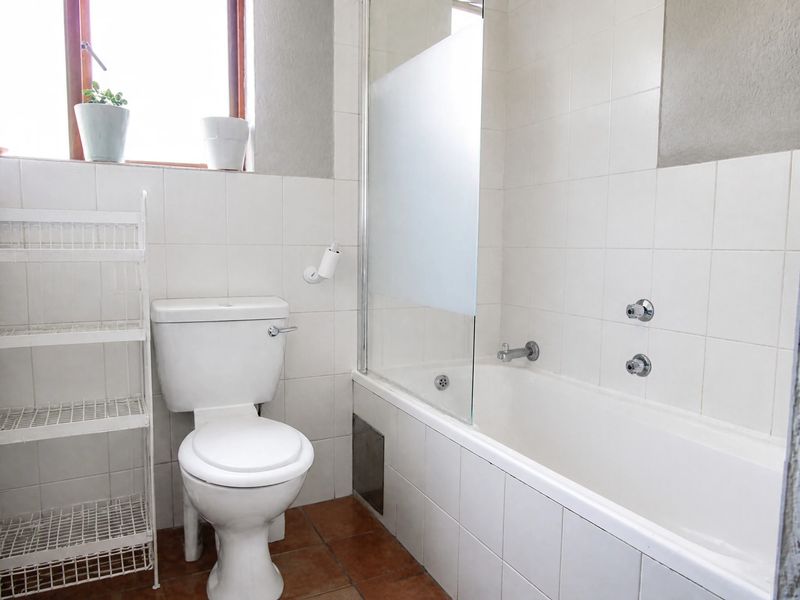 A functional bathroom featuring a white bathtub with a glass shower screen, a standard toilet, and neutral wall tiling.