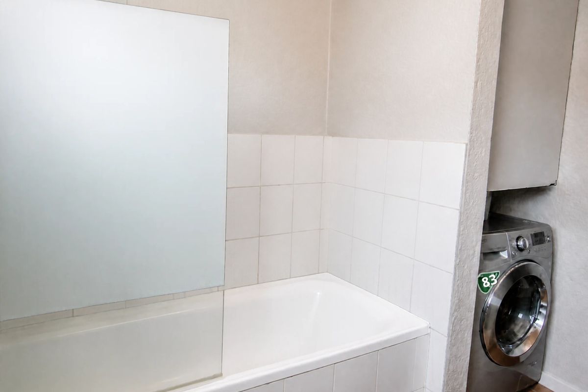 A functional bathroom featuring a built-in bathtub with a glass shower screen, tiled splashback, and a dedicated laundry area with built-in cabinetry.