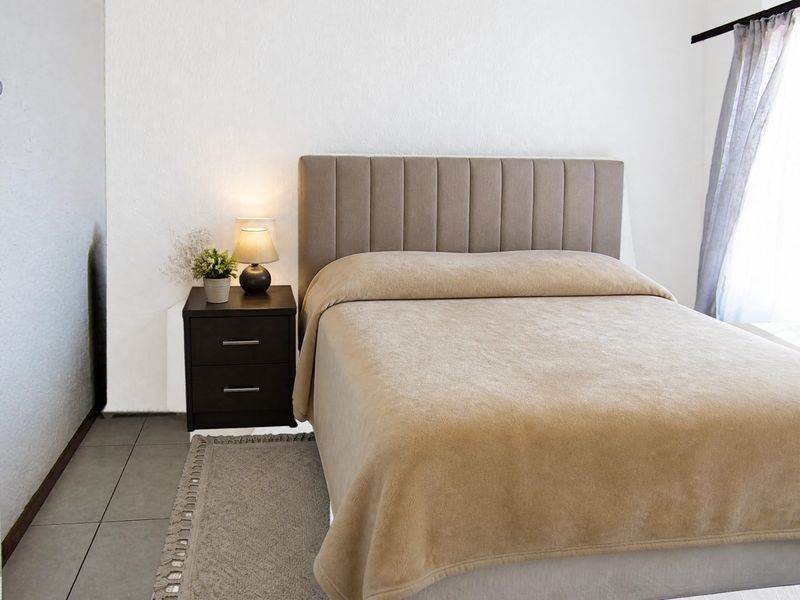 A well-maintained bedroom featuring neutral wall finishes, tiled flooring, and a modern upholstered headboard.