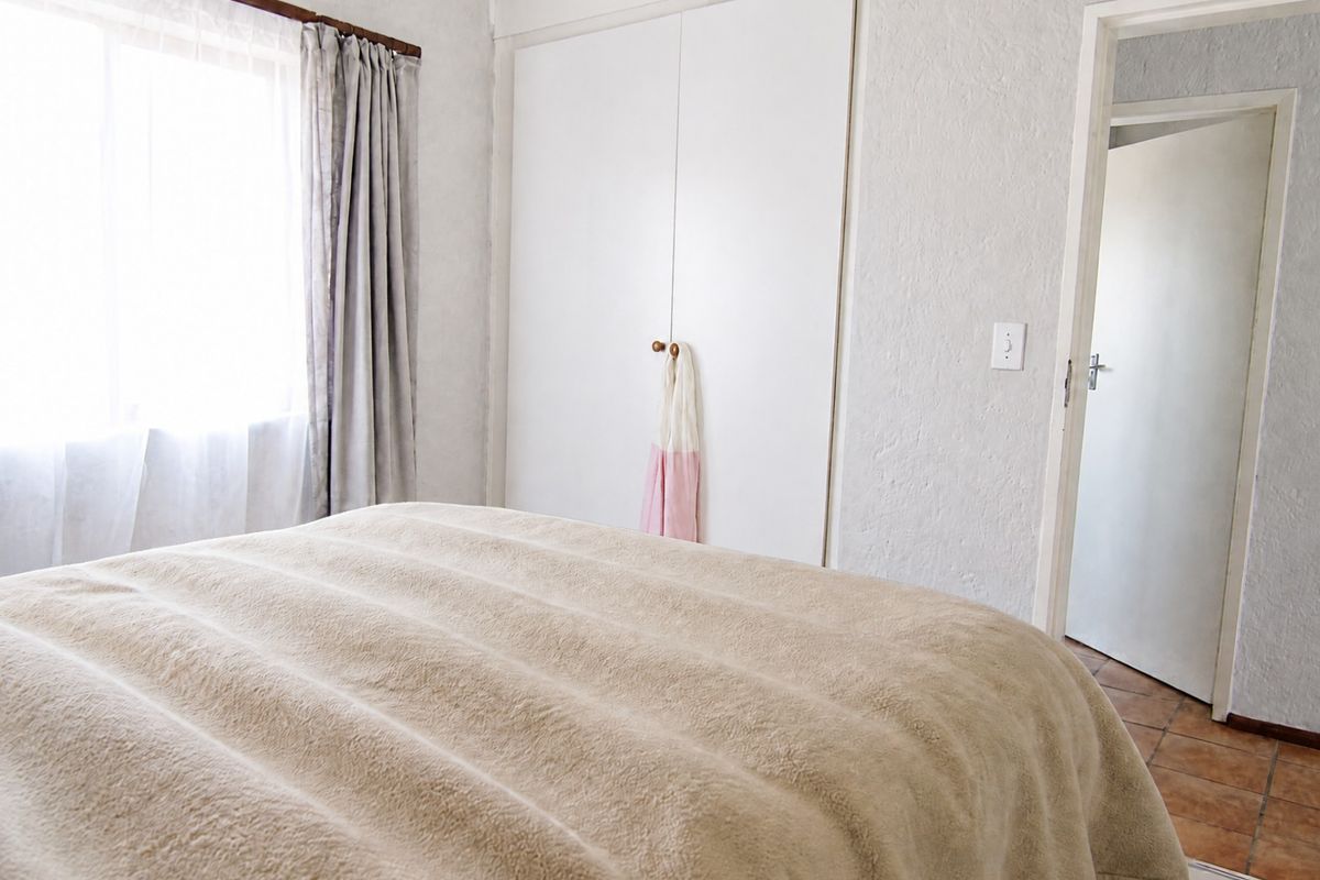 A functional bedroom featuring built-in cupboards, tiled flooring, and natural light from a sliding window.