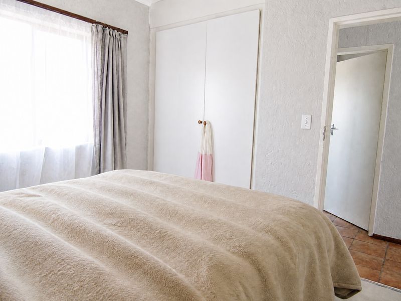 A functional bedroom featuring built-in cupboards, tiled flooring, and natural light from a sliding window.