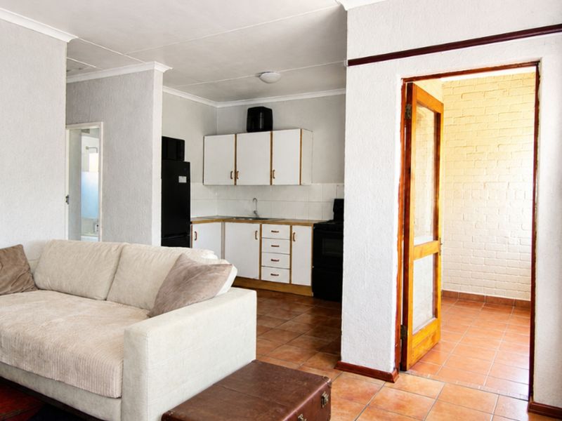 Open plan living area featuring a functional kitchen with built-in cabinetry and tiled flooring, leading to an adjacent room through a timber door frame.