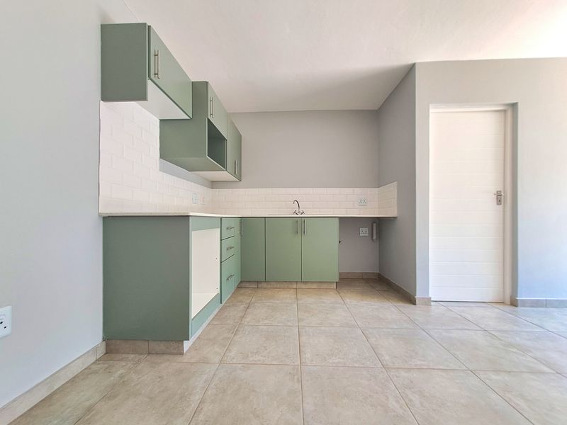 A clean, modern kitchen featuring sage green cabinetry, white subway tile backsplash, stone countertops, and neutral tiled flooring in an open-plan layout.