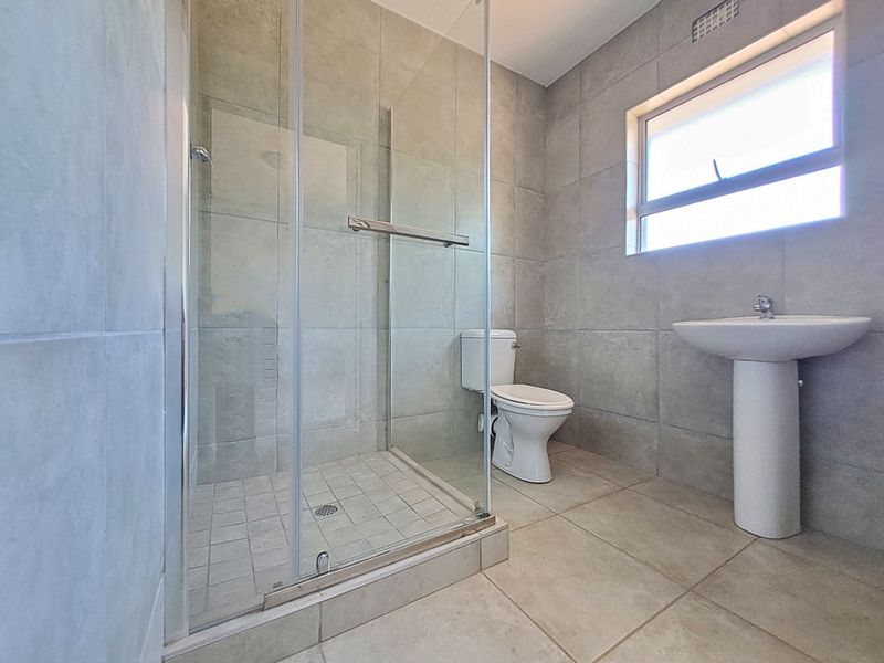 A clean and modern bathroom featuring a glass-enclosed shower, pedestal basin, and neutral floor-to-ceiling tiling.