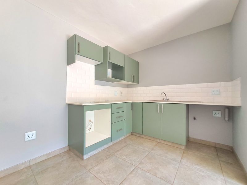 A clean, modern kitchen featuring sage green cabinetry, a white subway tile backsplash, tiled flooring, and a stainless steel sink.