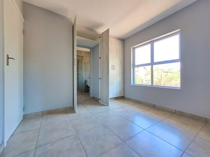 A bright, empty bedroom featuring neutral tiled flooring, built-in cupboards, and direct access to an en-suite bathroom.