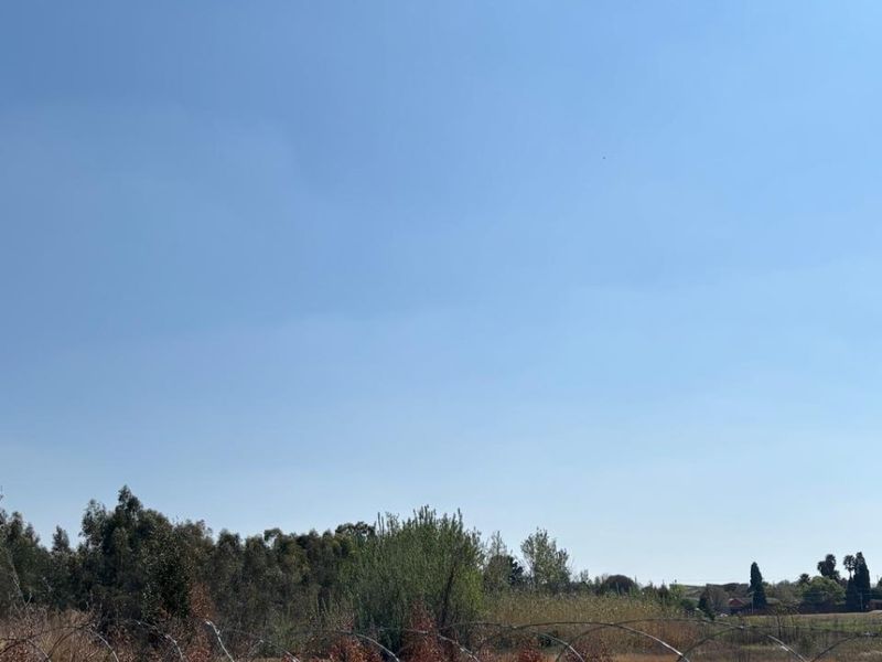 A view of a vacant commercial land plot featuring perimeter fencing with razor wire and natural vegetation.