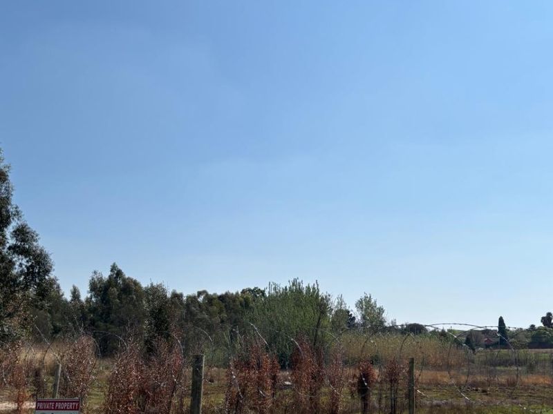 A view of a vacant commercial land plot secured with perimeter fencing and razor wire, featuring natural vegetation and clear sky.