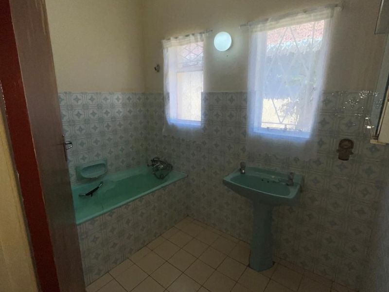 A dated bathroom featuring a pastel green pedestal basin and matching built-in bathtub, complemented by patterned wall tiles and neutral floor tiling.