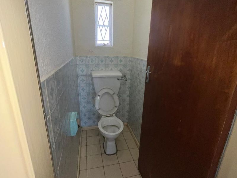 A compact, dated guest toilet featuring ceramic wall and floor tiles, a leaded glass window, and a standard white toilet suite.