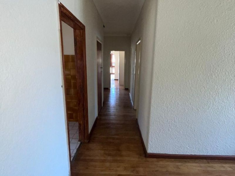 A vacant hallway featuring wooden flooring, coved ceilings, and access to multiple rooms, providing a clean canvas for interior design.