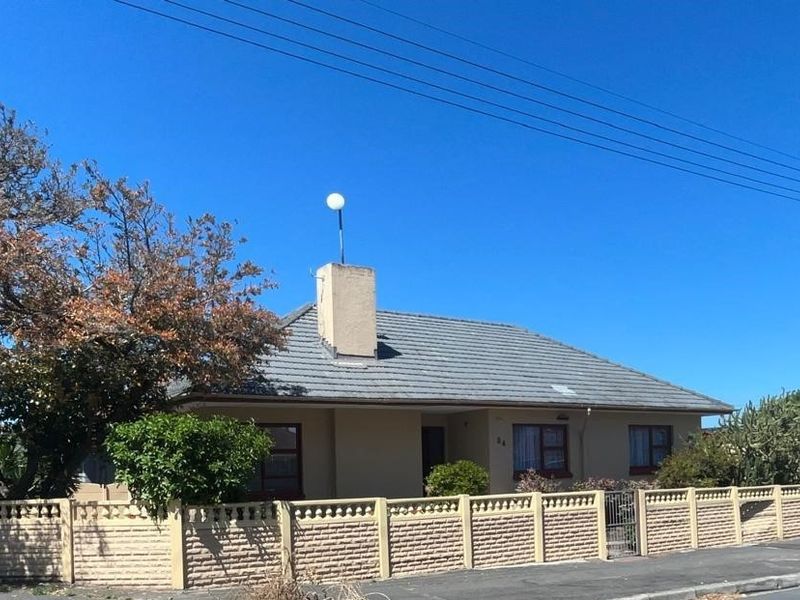 Front exterior view of a single-story house featuring a tiled roof, chimney, and a secure precast concrete boundary wall with a pedestrian gate.