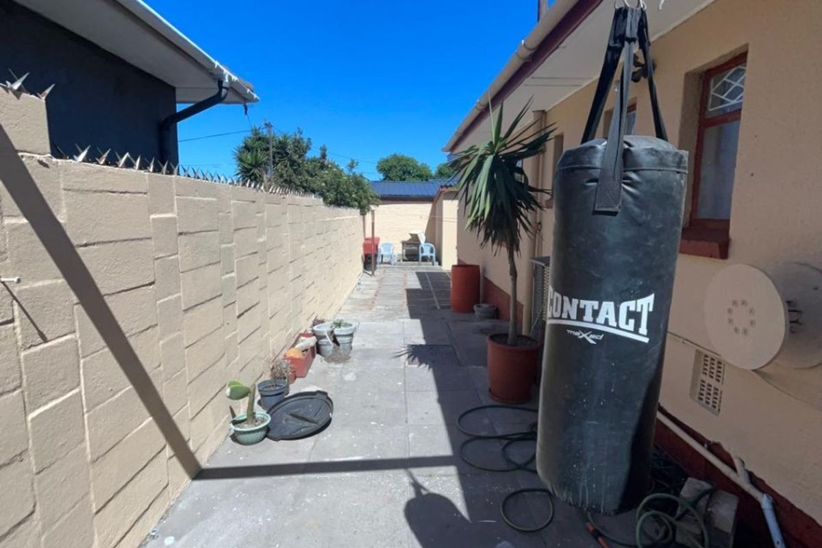 A narrow rear exterior walkway featuring a concrete block boundary wall with security spikes and paved flooring.