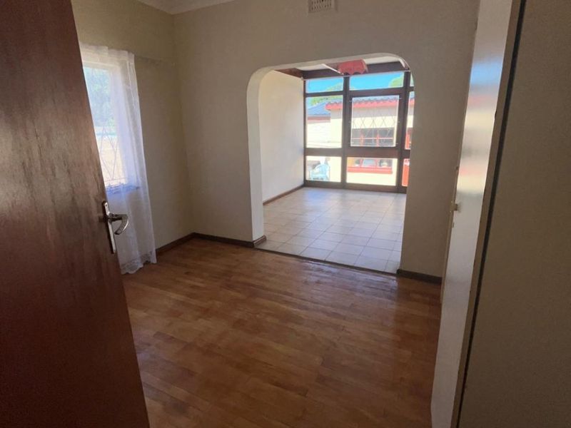 An empty living area featuring laminate flooring and an arched transition into a tiled sunroom, offering a bright and versatile living space.
