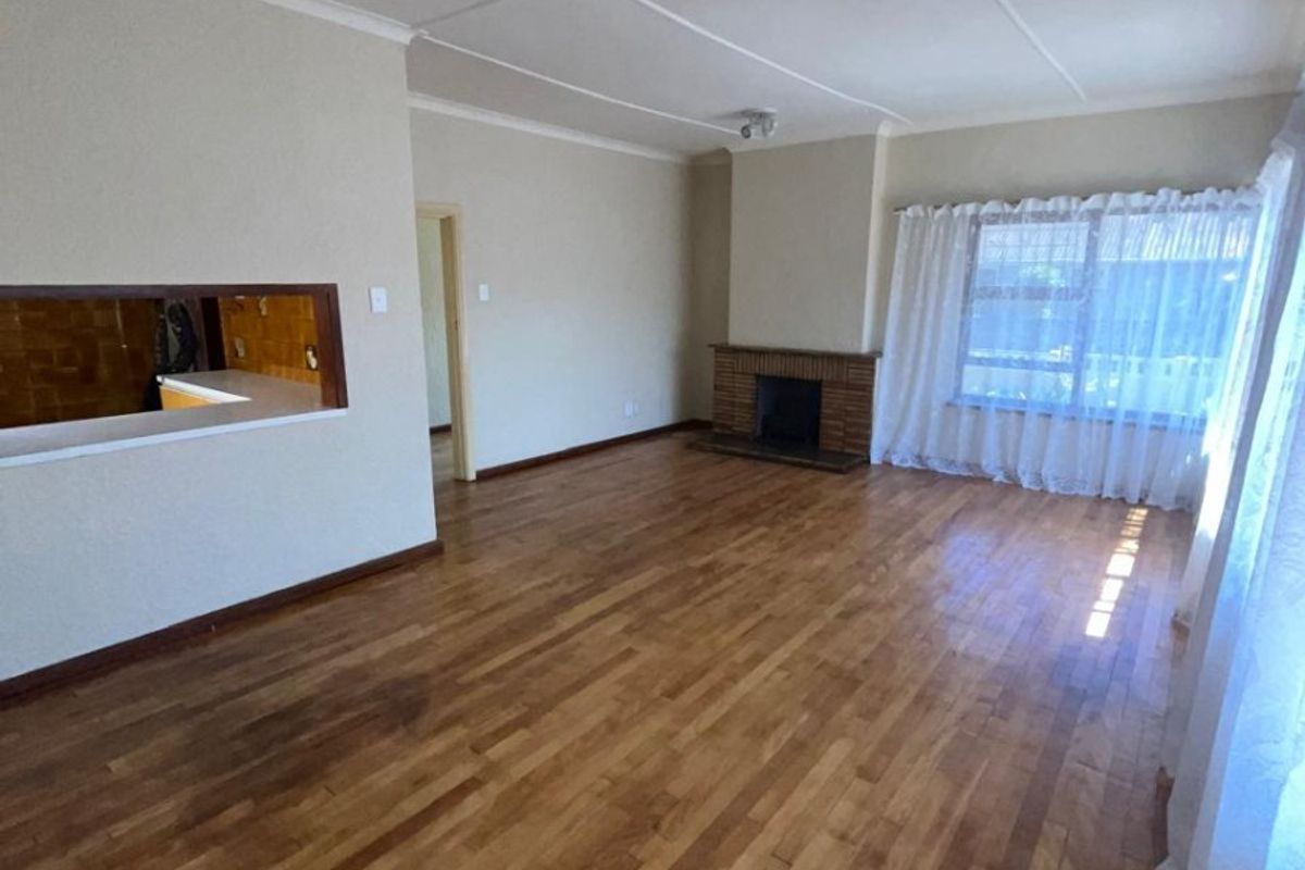 Spacious living room featuring original hardwood flooring, a classic brick fireplace, and a convenient serving hatch connecting to the kitchen area.