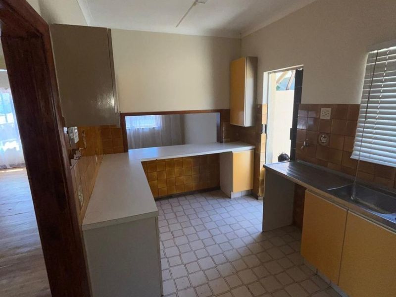 A functional, dated kitchen featuring original cabinetry, tiled backsplash, and tiled flooring, offering a blank canvas for modern renovation and design updates.