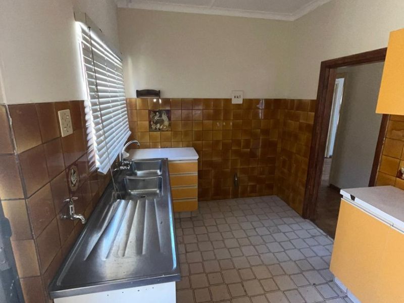 A functional kitchen space featuring a stainless steel double sink, tiled splashbacks, and original cabinetry, offering potential for a modern renovation.