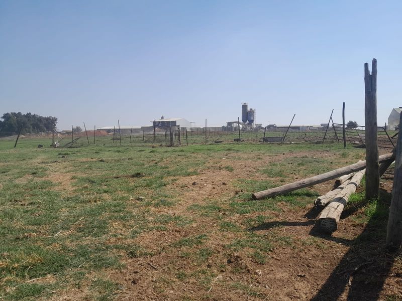 An expansive open farm field featuring wire fencing and wooden posts, with industrial structures visible in the distance.