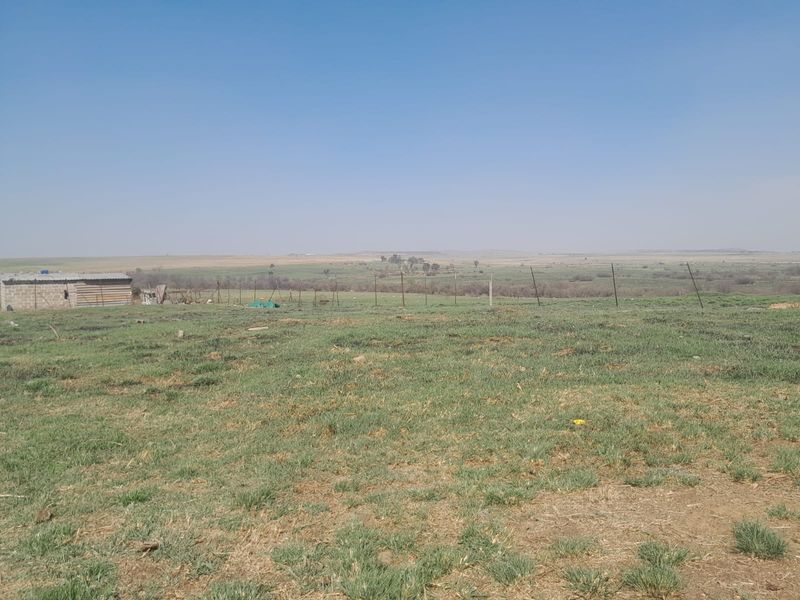 Expansive view of open farm land featuring wire fencing and a small outbuilding structure under a clear sky.