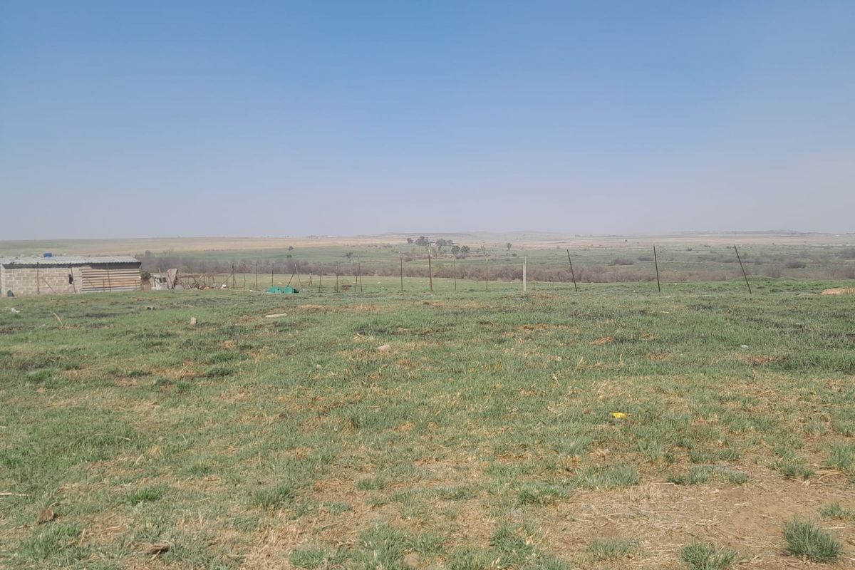 Expansive view of open farm land featuring wire fencing and a small outbuilding structure under a clear sky.