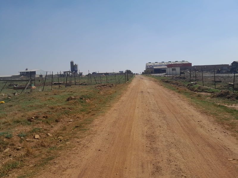 A view of a dirt access road leading towards industrial farm buildings and infrastructure under a clear sky.