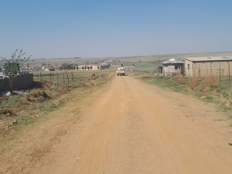 A view of a rural dirt access road leading towards distant farm structures and open landscape.