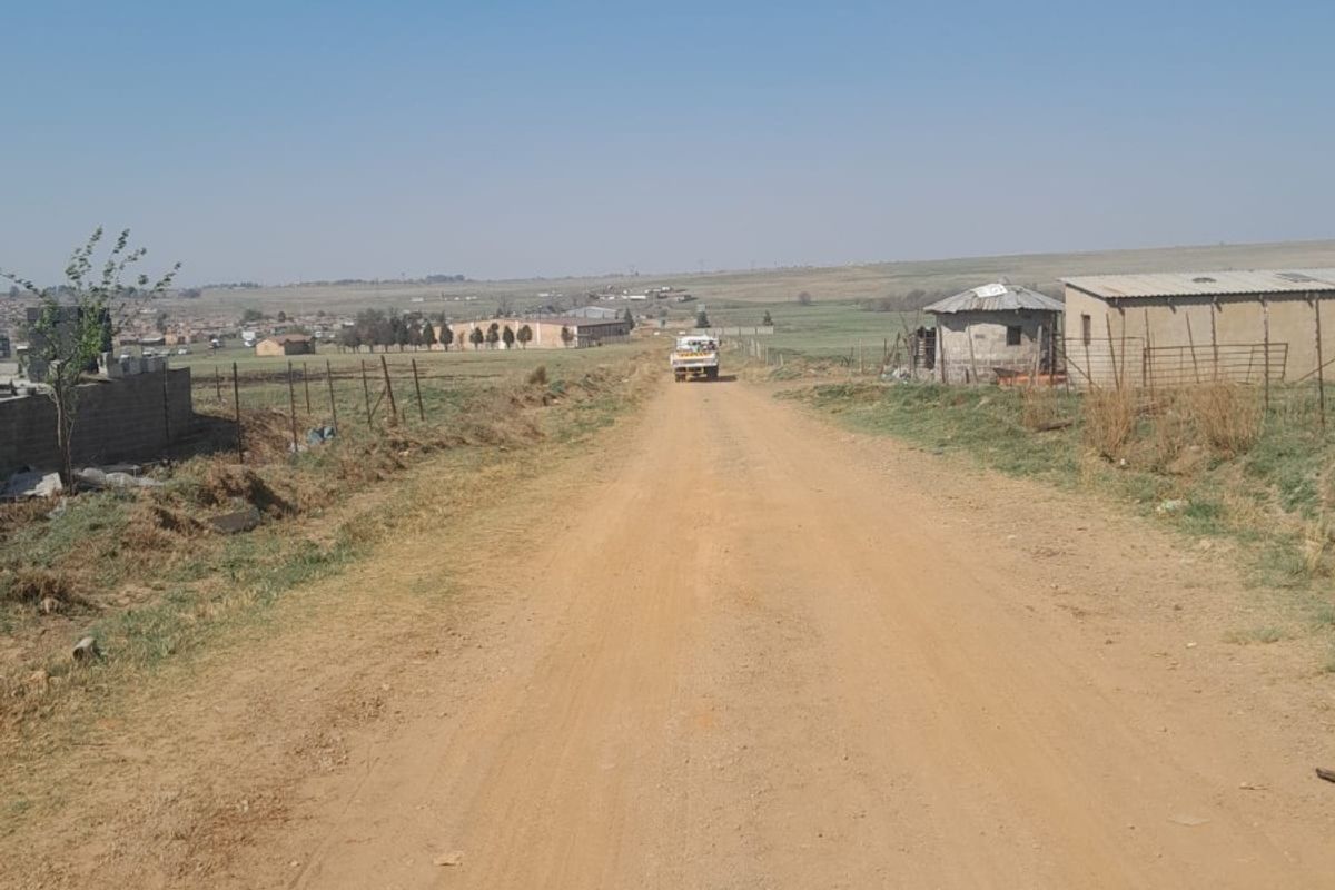 A view of a rural dirt access road leading towards distant farm structures and open landscape.