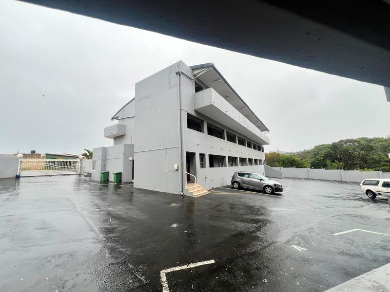Exterior view of a multi-story apartment building featuring a paved parking area, concrete facade, and private balconies.