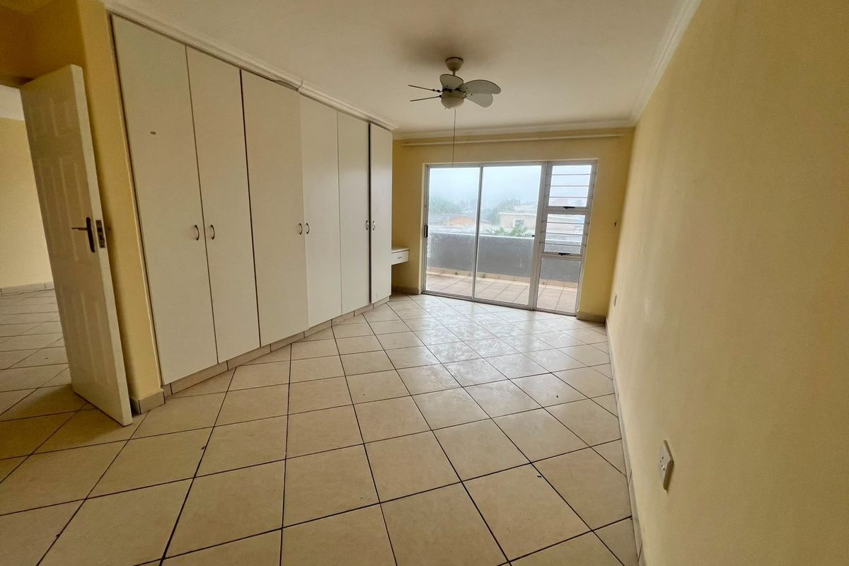 Spacious bedroom featuring built-in cupboards, tiled flooring, a ceiling fan, and direct access to a private balcony through sliding glass doors.