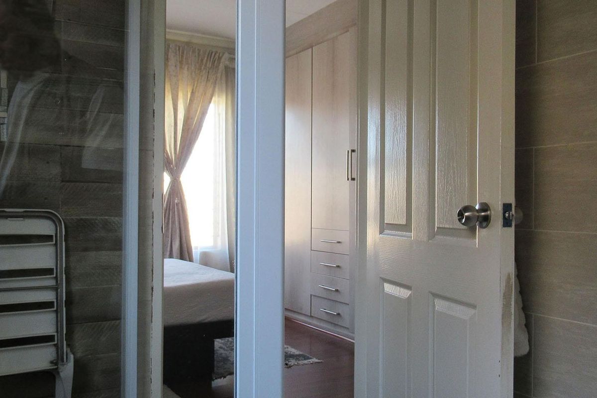 A view through a doorway into a bedroom featuring built-in cupboards and laminate flooring, with tiled wall finishes visible in the foreground.