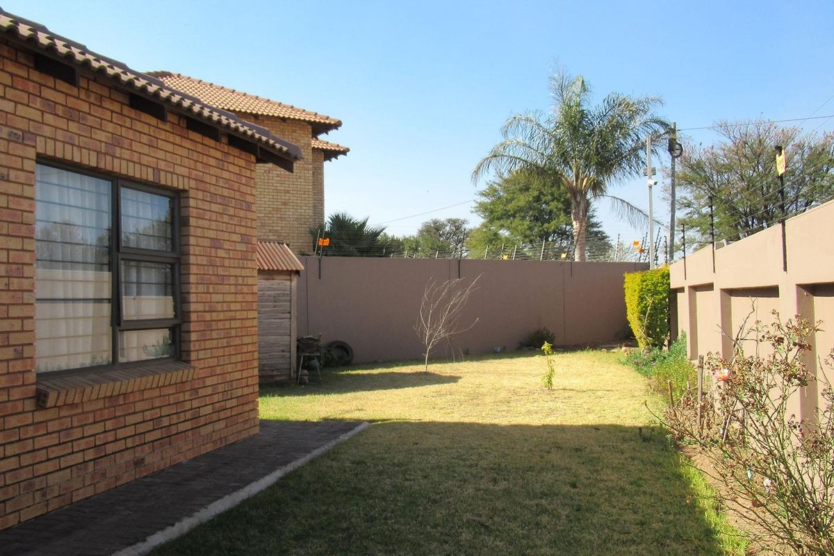 A view of the rear garden featuring a face brick exterior, paved walkway, and secure perimeter walling.