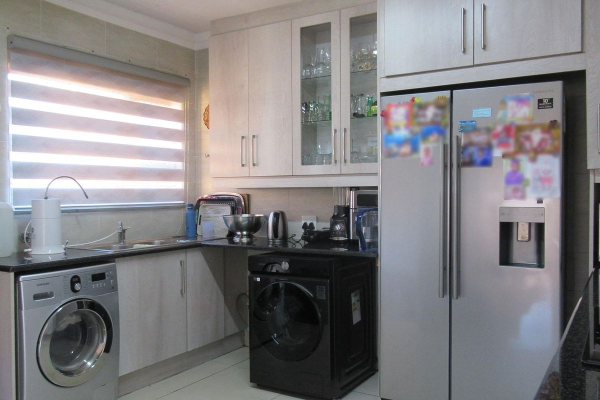 A functional kitchen featuring light-toned built-in cabinetry, granite countertops, tiled backsplash, and integrated space for laundry appliances.