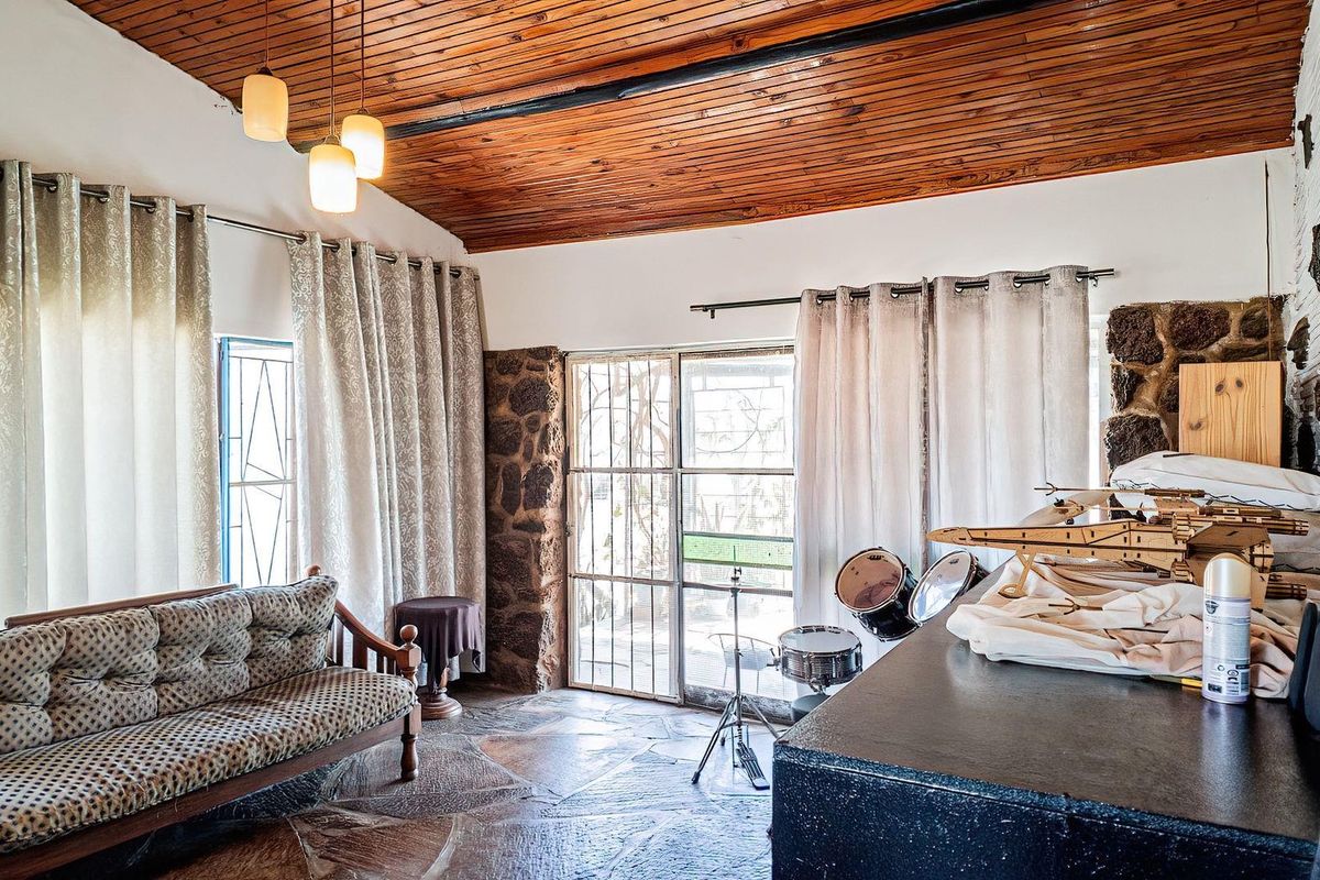 A rustic living room featuring a timber plank ceiling, flagstone flooring, and exposed stone wall accents with direct access to the exterior.