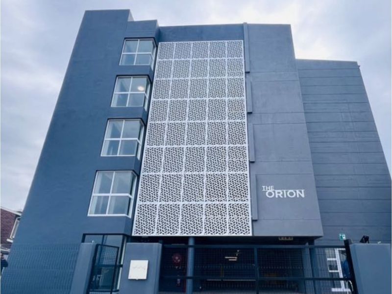 Front elevation of The Orion apartment building, featuring a modern blue facade with decorative metal screening and secure gated access.