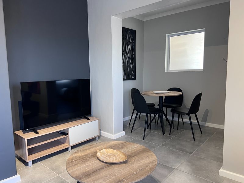 An open-plan living and dining area featuring modern grey floor tiles and a dark accent wall, creating a contemporary and cohesive living space.