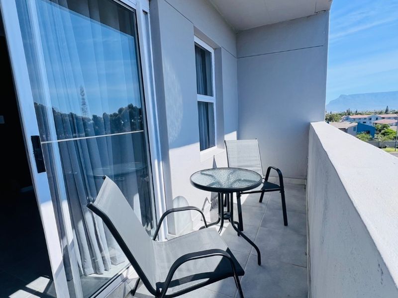 A clean, covered balcony featuring tiled flooring, a sliding glass door entrance, and a solid concrete balustrade with views of the surrounding area.