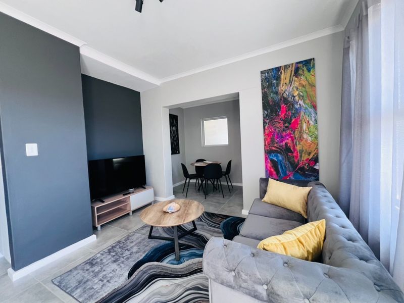An open-plan living and dining area featuring tiled flooring, a dark feature wall, and neutral finishes, creating a bright and functional living space.