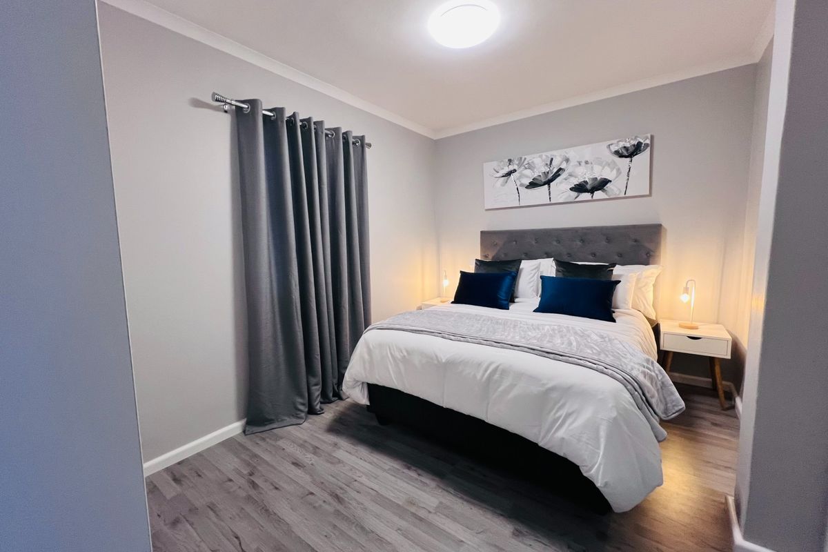 A well-maintained bedroom featuring modern grey laminate flooring, neutral wall tones, and a flush mount ceiling light fixture.