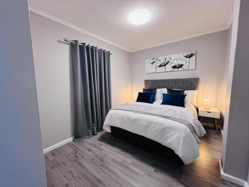 A well-maintained bedroom featuring modern grey laminate flooring, neutral wall tones, and a flush mount ceiling light fixture.