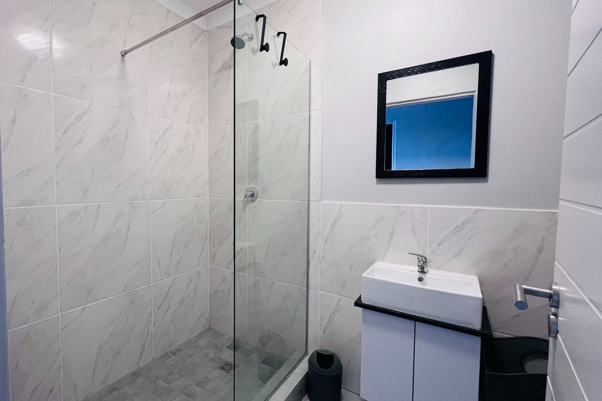 Modern bathroom featuring a walk-in shower with glass screen, marble-look wall tiling, and a sleek wall-mounted vanity with a ceramic basin.