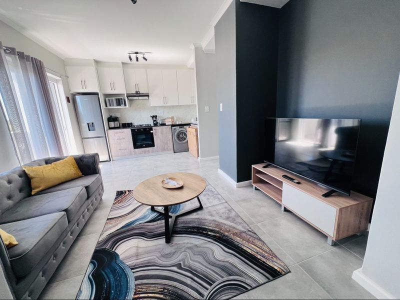 Modern open-plan living area featuring a contemporary kitchen with built-in appliances, tiled flooring, and a seamless transition to the lounge space.