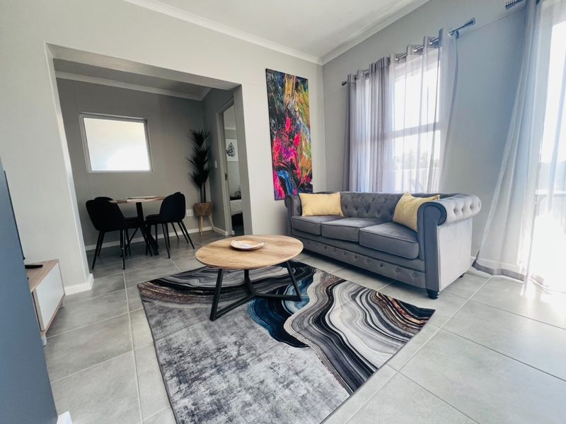 Bright open-plan living and dining area featuring neutral tiled flooring, modern finishes, and natural light through large windows.