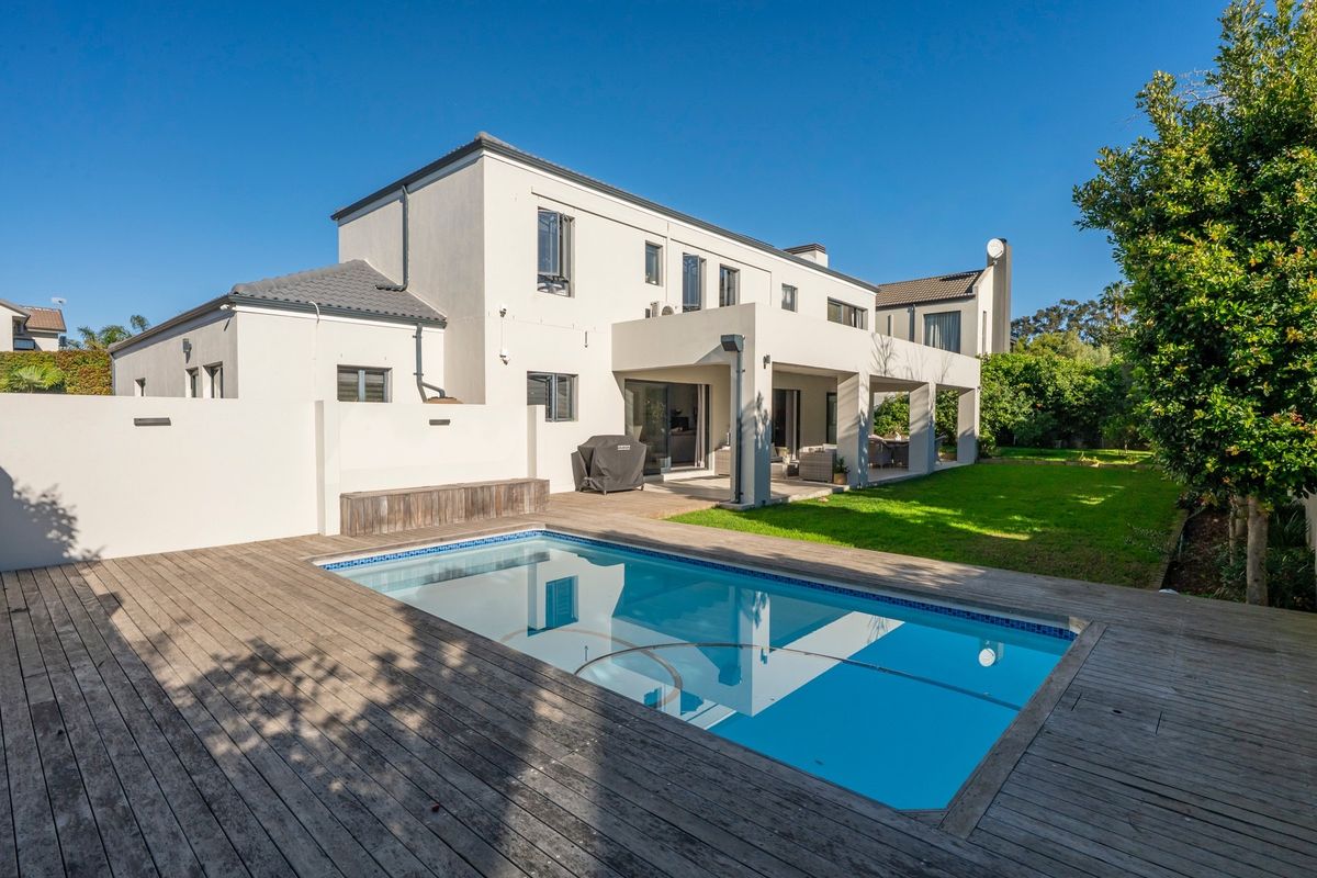 Rear view of the property featuring a swimming pool, timber decking, and a spacious covered patio overlooking the landscaped garden.