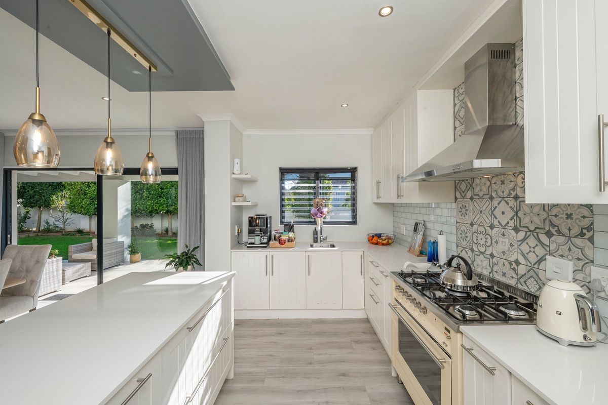 Modern kitchen featuring shaker-style cabinetry, quartz countertops, a gas hob with extractor, and a central island, seamlessly flowing to an outdoor patio area.
