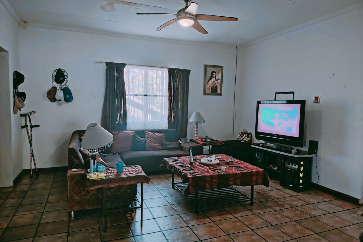 A living room featuring tiled flooring and a ceiling fan, showing signs of ceiling water damage.